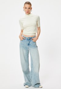 Witte getailleerde short-sleeve top met een kraag, gecombineerd met lichtblauwe wijde jeans met een vervaagde wassing en een klassieke vijf-pocket stijl.