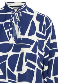 Tunic blu e bianca con motivo geometrico, tessuto morbido, collo alto e chiusura a cravatta al collo, con maniche lunghe e vestibilità rilassata.