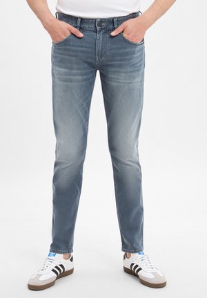 Light blue denim jeans with a slim fit, featuring a button closure and five pockets; worn with white sneakers with black stripes.