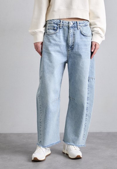 Lyseblå, brede jeans med løs pasform, der har fem lommer, kontrastsyer og frynsede kantkanter. Bæres med hvide sneakers.