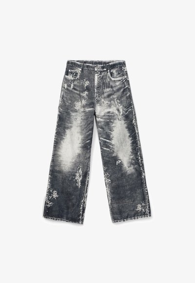 Jeans larges délavés noir et blanc avec plusieurs patchs effilochés et ourlet brut, étalés à plat sur un fond blanc.