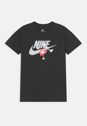 Sort Nike T-shirt med stort sølv Nike-logo og en rød animeret figur iført sneakers integreret i designet på brystet.