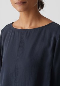 Blusa blu navy con scollatura rotonda, texture plissettata e cucitura centrale. Realizzata in tessuto leggero, offre una finitura liscia.