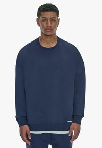 Marineblå sweatshirt med rund hals, nedsatte skuldre, ribbede manchetter og et rent design. Blød tekstur med minimal branding ved kanten.