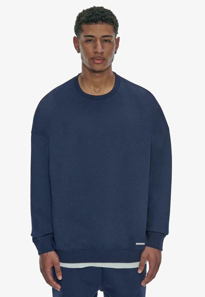 Marineblå sweatshirt med rund hals, nedsatte skuldre, ribbede manchetter og et rent design. Blød tekstur med minimal branding ved kanten.