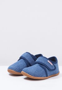 Niebieskie tekstylne buty wsuwane z elastycznymi paskami, teksturowanymi materiałami i jasnobrązowymi gumowymi podeszwami, z delikatnymi wzorami i zaokrąglonym kształtem.