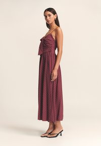 Bordowa sukienka w białe groszki, bez rękawów, z marszczonym gorsetem, zwiewną spódnicą o długości do połowy łydki, w połączeniu z czarnymi sandałami na niskim obcasie.