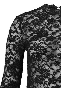 Svart spetsblus med långa ärmar, hög krage, blommönster, genomskinlig textur och detaljerad sömnad längs kragen.