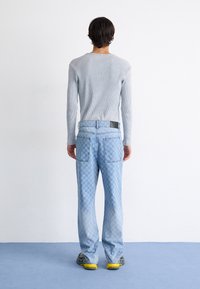 Lys grå ribbet langermet topp, parret med blå denim jeans med rutemønster, vist fra baksiden.