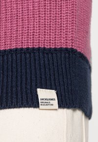 Knit sweater featuring a pink and navy striped pattern, with a ribbed navy hem and a branded label sewn at the bottom edge.