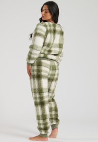 Fleece loungewear set in green and white plaid, featuring a round neckline, long sleeves, ribbed cuffs, and elastic waistband for comfort.