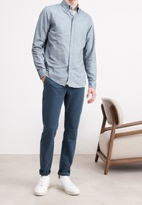 Ljusblå skjorta med knappar, marinblå byxor och vita sneakers. Skjortan har en slät yta med knappar och långärmar, skräddarsydd passform.