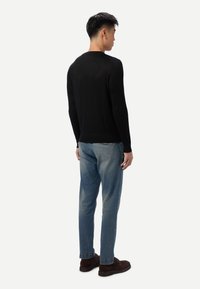 Pull en maille noire à manches longues, associé à un jean bleu clair et des chaussures marron, vu de dos. Texture lisse, coupe ajustée.