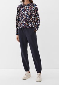 Top scuro a motivo floreale con maniche lunghe, abbinato a pantaloni blu navy con polsini elasticizzati e sneaker chiare. Tessuto dalla superficie liscia.