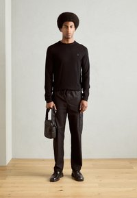 Black long-sleeve shirt with small logo, paired with black drawstring cargo pants. Accessories include a compact black shoulder bag. Classic leather shoes.