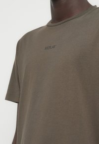 Λαδί βαμβακερό t-shirt με κοντά μανίκια, με διακριτικό τύπωμα "REPLAY" σε μαύρο χρώμα στο κέντρο του στήθους. Μαλακή υφή.