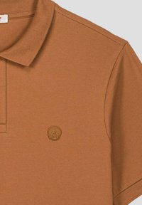 Polo in cotone marrone con collo a costine, maniche corte e patch con logo in gomma sul petto. Tessuto strutturato con trama sottile.