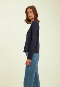 Pull en maille bleu marine à manches longues, offrant une coupe décontractée et des poignets côtelés. Associé à un jean bleu clair taille haute.
