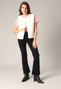 Witte nepbont vest met een rechte snit, gedragen over een roze T-shirt en gecombineerd met zwarte flared jeans en zwarte enkellaarsjes.