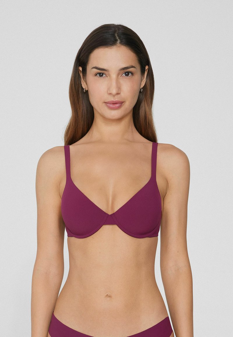 Soutien-gorge bordeaux rembourré avec bretelles ajustables, une texture lisse et une forme de cup triangulaire, conçu pour le confort et le soutien.