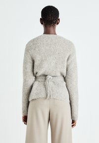 Pulover tricotat de culoare gri deschis, cu o cravată la talie, având o textură moale și un decolteu rotund, asortat cu pantaloni largi de culoare bej.