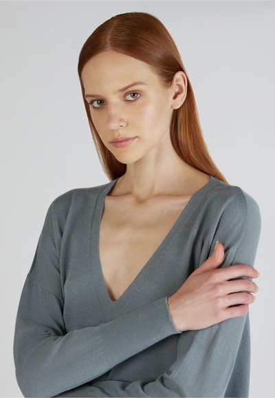 Hellgrauer V-Ausschnitt-Pullover mit langen Ärmeln, strukturiertem Strick und lockerer Passform. Auffälliger tiefer Ausschnitt und weicher Stoff.