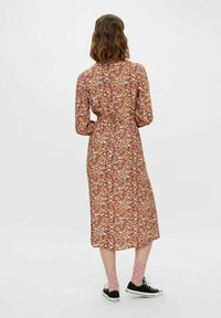 Abito floreale a metà lunghezza con maniche lunghe, vita stretta e un motivo multicolore su uno sfondo chiaro. Indossato con calzini rosa a pois e sneakers nere.