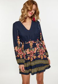 Rochie bleu marin cu mâneci lungi, decolteu în V, talie strânsă și broderie florală intricate în roșu și galben, evidențiind o fustă stratificată.