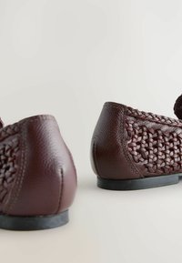 Chaussures en cuir bordeaux avec un texture tissée sur les côtés, orteils arrondis et petits talons noirs, ornées de détails de couture délicats.