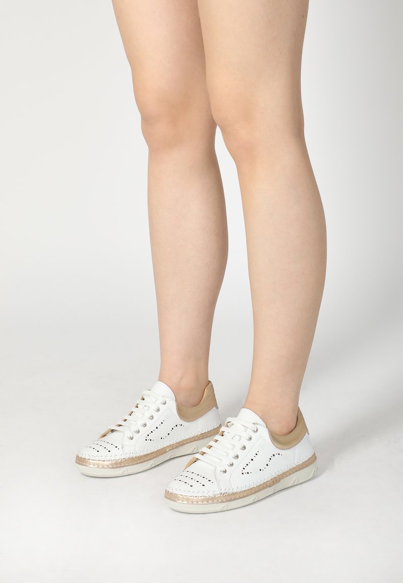 Weiße Leder-Sneaker mit durchlöchertem Design, beigen Akzenten und gewebten Texturen um die Sohle. Abgerundete Zehenform und flache Gummisohle.