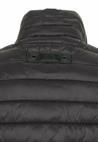 Chaqueta de plumón negra acolchada por detrás, con cuello alto y un pequeño parche rectangular cosido en la parte superior central.