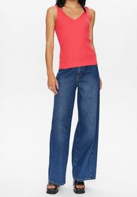 Korallfärgad ribbad linne med v-ringning, kombinerad med vida mörkblå denimjeans och svarta platåsandaler. Enkel och avslappnad design.