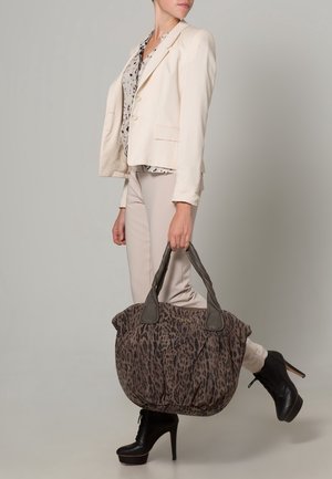 Grand sac en tissu à imprimé léopard avec des poignées gris foncé, associé à un blazer crème et un pantalon beige, porté avec des bottes noires à talons hauts.