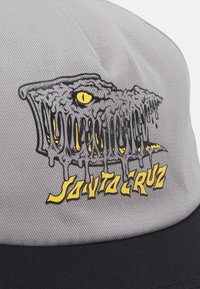 Grijze pet met een afbeelding van een druipende monster mond in zwart en geel, met de tekst "Santa Cruz" in vetgedrukt gele letters.