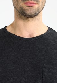 Mörkgrå kortärmad t-shirt med rund halsringning och en liten bröstficka, tillverkad av ett mjukt, texturerat tyg.