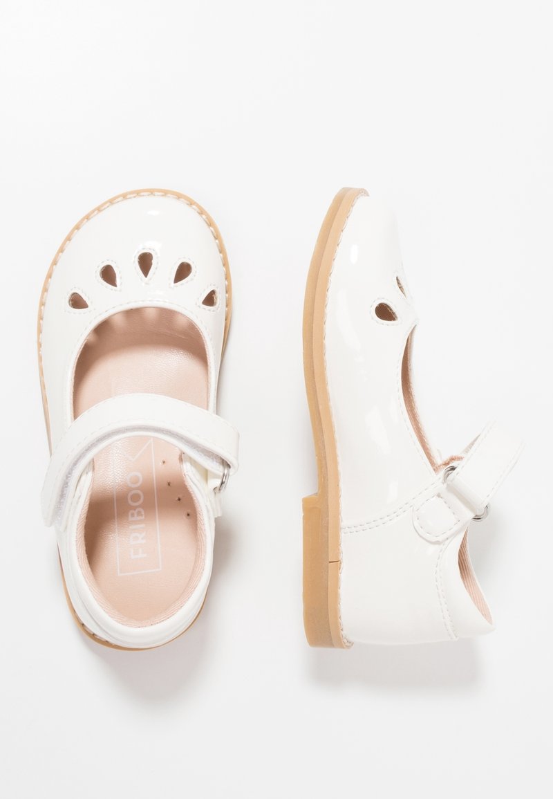 Białe lakierowane buty typu Mary Jane z okrągłym noskiem, wyciętym kwiatowym wzorem, paseczkiem wokół kostki oraz beżową gumową podeszwą. Gładka tekstura.