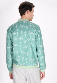 Groene bomberjack met paard- en cactuspatter, voorzien van een geribbelde kraag en manchetten, een gladde textuur en een elastische tailleband.