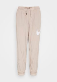 Beige leichte Jogginghosen mit elastischem Bund, verstellbarem Kordelzug und weißem Nike Swoosh-Logo am linken Bein. Mit Bündchen an den Knöcheln.