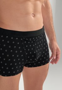 Schwarze Boxershorts mit einem gemusterten Design, das kleine sechseckige Formen in Hellblau und Beige zeigt. Elastischer Bund mit Markenlogo.