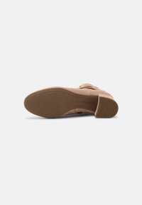 Semelle d'une chaussure femme beige avec semelle texturée antidérapante, petit talon bloc et boucle décorative sur la partie supérieure.