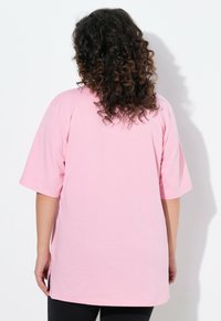 Helles rosa, übergroßes T-Shirt mit kurzen Ärmeln, aus weichem Stoff, mit einem runden Ausschnitt und lässiger Passform, von hinten betrachtet.