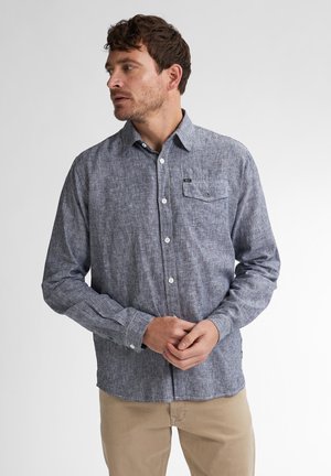 Camisa de botones a rayas azul y blanca, con manguitas largas, un bolsillo en el pecho y botones blancos, hecha de una tela ligera y texturizada.