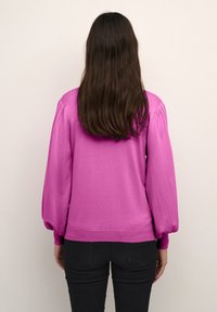 Magenta Pullover mit puffärmeln und schmalem Ripp-Hem; aus weichem Stoff; über schwarzen Hosen getragen; verfügt über eine glatte Textur.