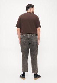 Tricou din bumbac maro, croi lejer. Jeans din denim gri-maro, formă tapered cu buzunare din spate vizibile. Adidași negri cu talpă din cauciuc.