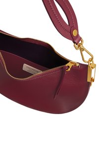 Borsa in pelle bordeaux con zip dorata, tasca interna e dettagli in oro. Forma curva e superficie testurizzata con una tracolla removibile.