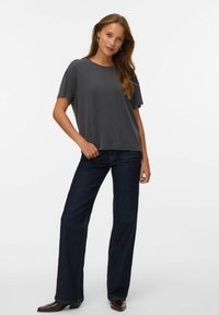 Grå kortærmet t-shirt med rund hals, båret med mørkeblå flared jeans. Stofoverfladen virker glat, og pasformen er afslappet.