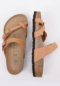 Tan leather sandals with two adjustable straps, cork footbed, textured light brown outsole, and subtle embossed branding on the insole.