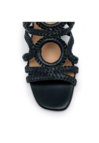 Sandale noire à lanières avec des lanières tissées ornées d'accents circulaires, design à bout ouvert et finition en cuir texturé. La semelle est lisse et plate.