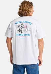 White cotton t-shirt featuring a graphic of a striped surfer with a surfboard, blue text reading "WAVE MAGNET" and "Call 617-BONG."