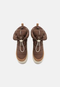Botas aisladas marrones con un diseño acolchado, acentos de ante sintético y un sistema de cordones blanco, con una suela de goma beige y detalles del logo.